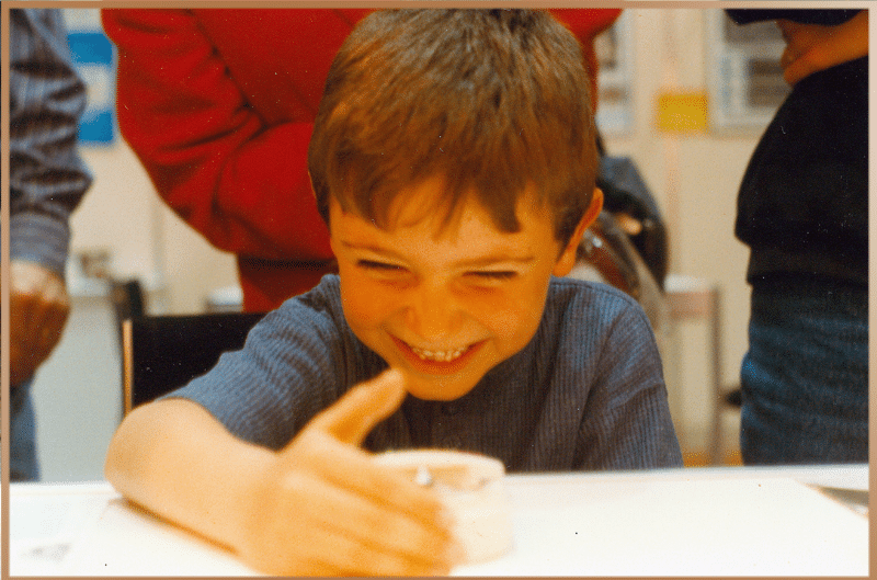 A boy laughs while measuring his vitality using a device, embodying the connection between humor and increased life energy.